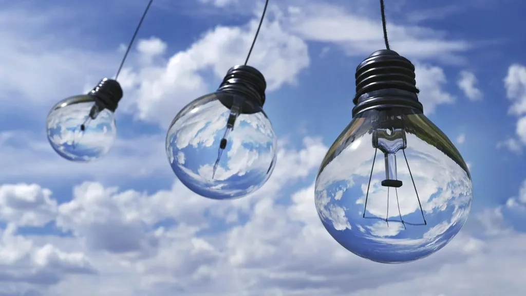Light bulbs hanging in a row with a cloudy blue sky in the background.