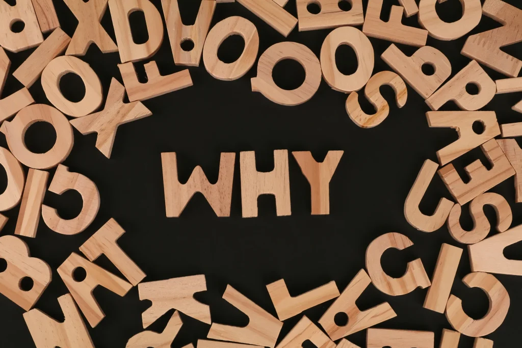 Over a black background, wooden letters are scattered. In the middle, the letters 'WHY" appear with negative space around it, separating the formed word from the other lone letters.