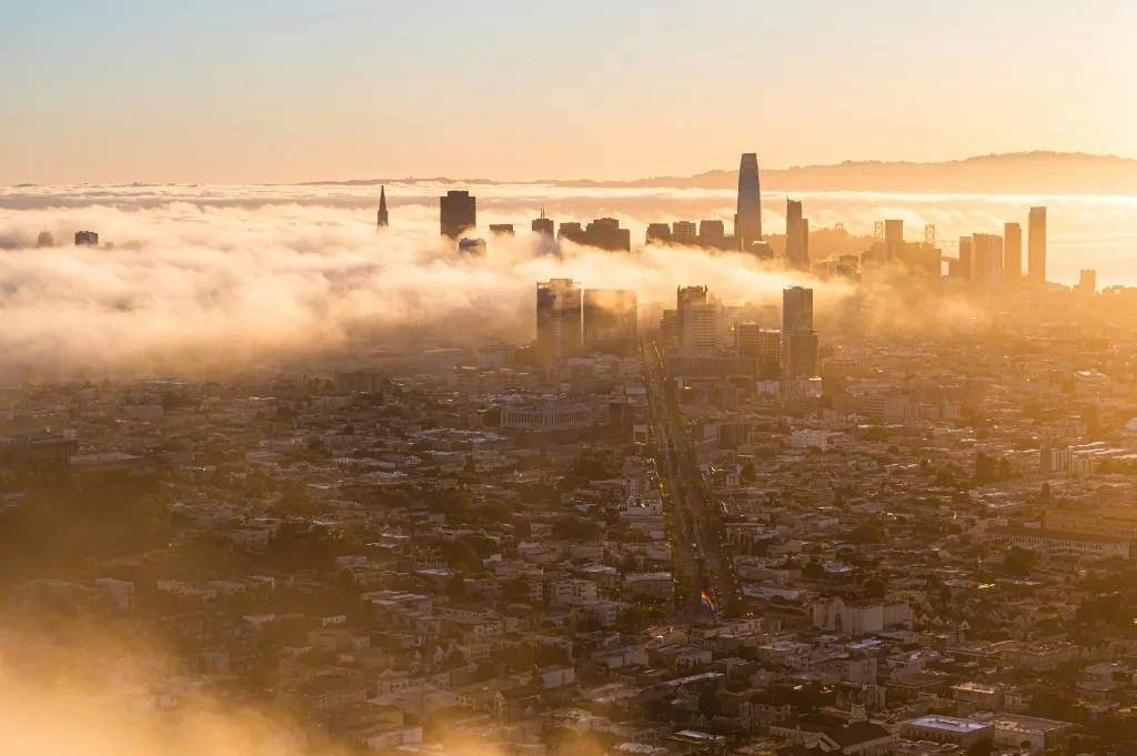 A photo of the smog in Silicon Valley during golden hour. City's tallest buildings peak through clouds. 