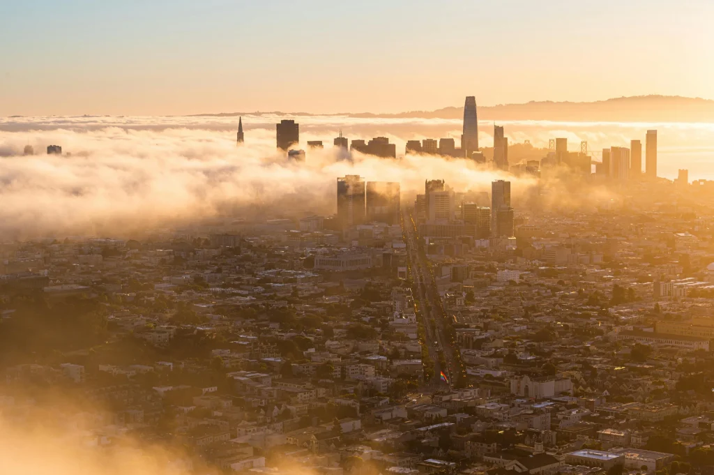 A photo of the smog in Silicon Valley during golden hour. City's tallest buildings peak through clouds. 