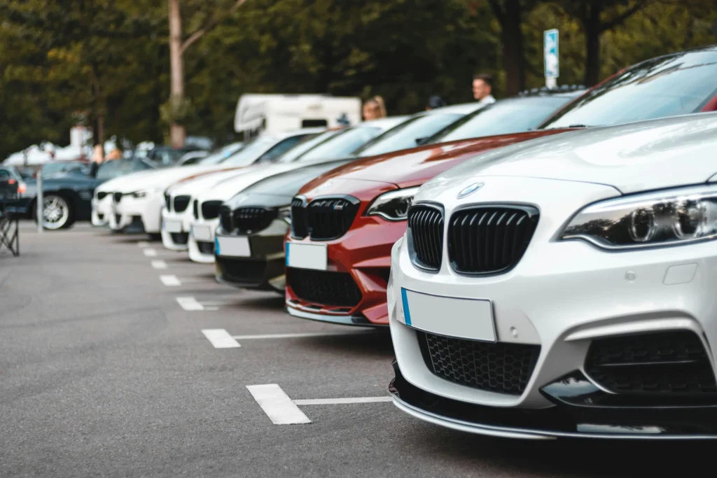 A row of BMW cars are parked in a parking lot, pictured up close to one of the grills, diagonally so that you can see many cars are parked beside it.