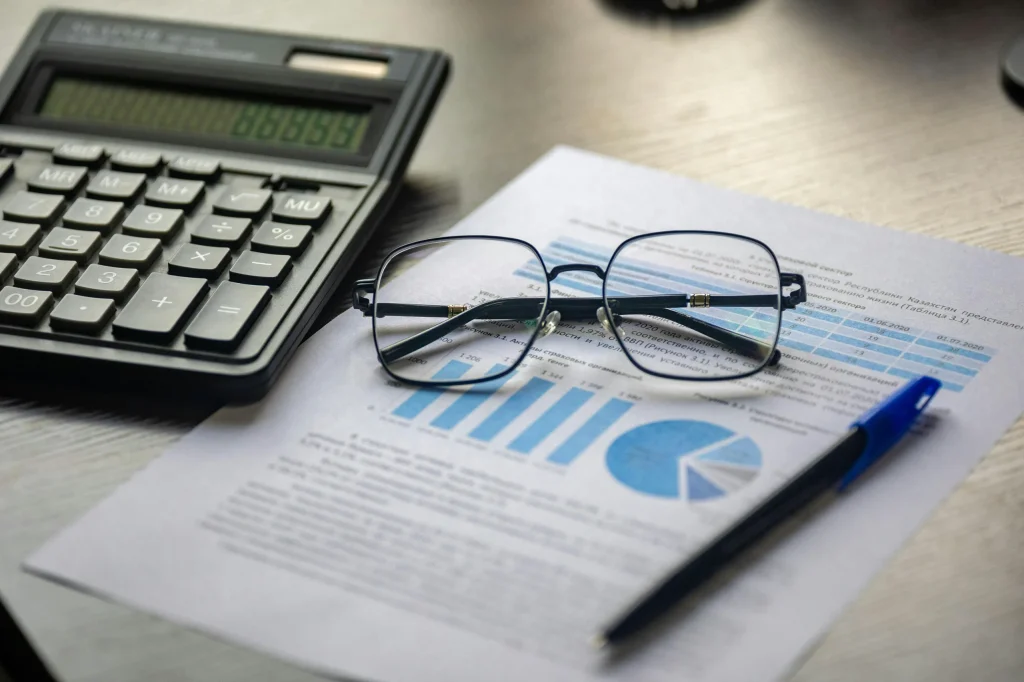 Glasses are folded above a graph or chart of some kind, which is printed on paper. A calculator is laying beside it. 