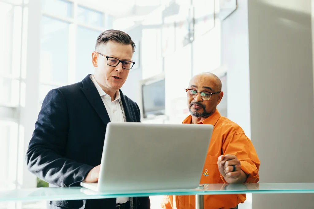 Two men discussing commission sales tax over a laptop on a glass desk. 