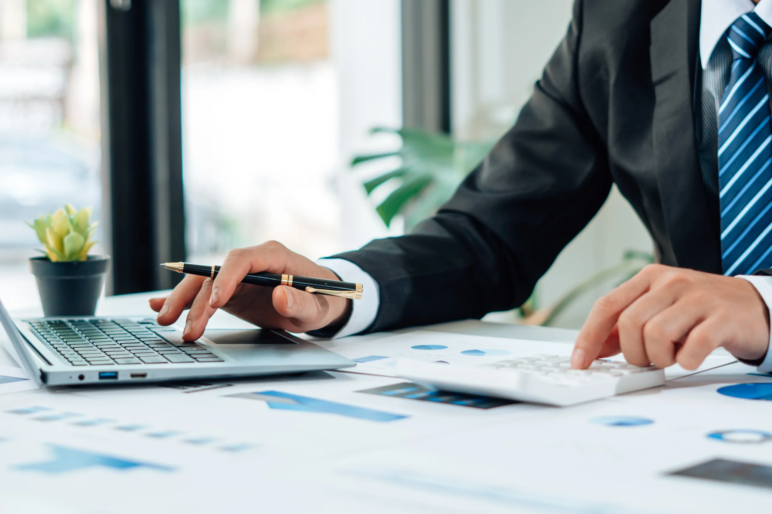 Outsourced financial controller services at Simplicity Financial An outsourced financial controller typing on a laptop and arranging stationary on a desk as they service clients remotely